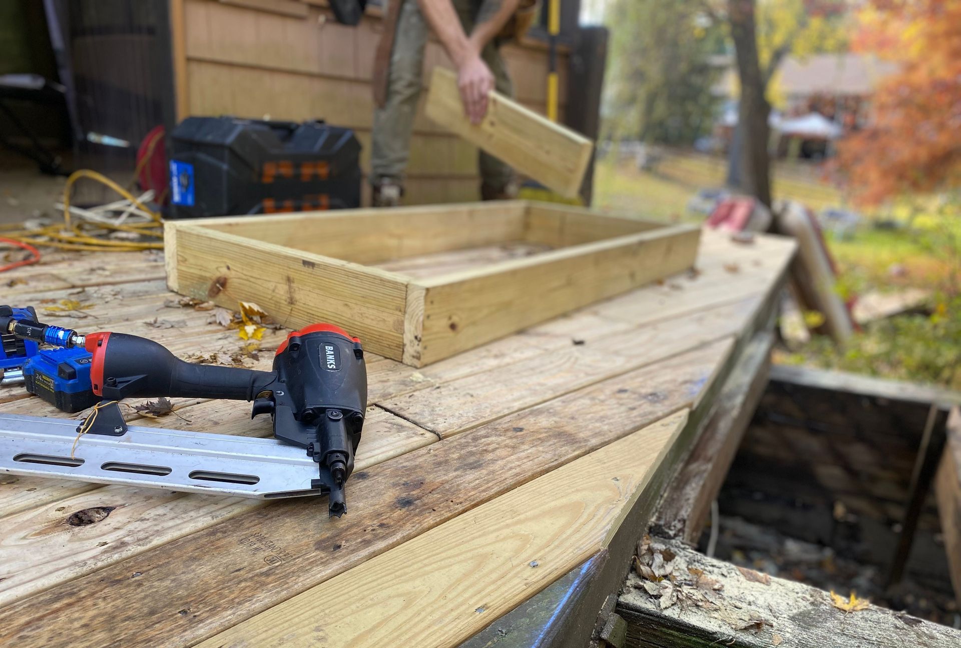 Close-up of carpentry work on a deck with a nail gun and wooden frame under construction.